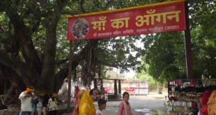 माँ कामाख्या धाम, गहमर, गाजीपुर के मंदिर परिसर में स्थित विशाल वटवृक्ष के नीचे नया बना छायेदार स्थान 'माँ का आँगन'। तस्वीर में लाल रंग का स्वागत बोर्ड, बरगद का पेड़ और श्रद्धालु दिखाई दे रहे हैं।"